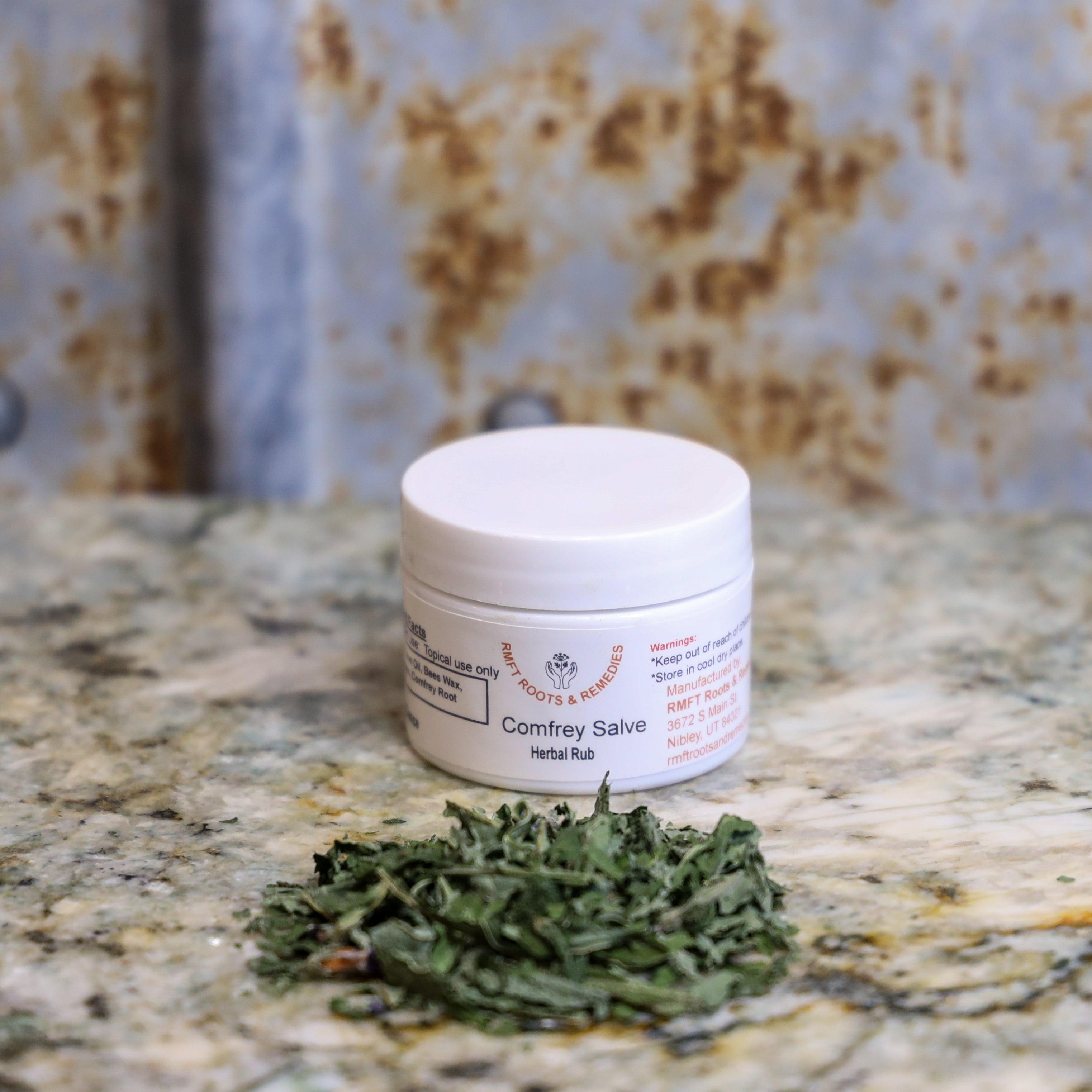 Jar of Comfrey Salve on a marble surface with dried comfrey leaves