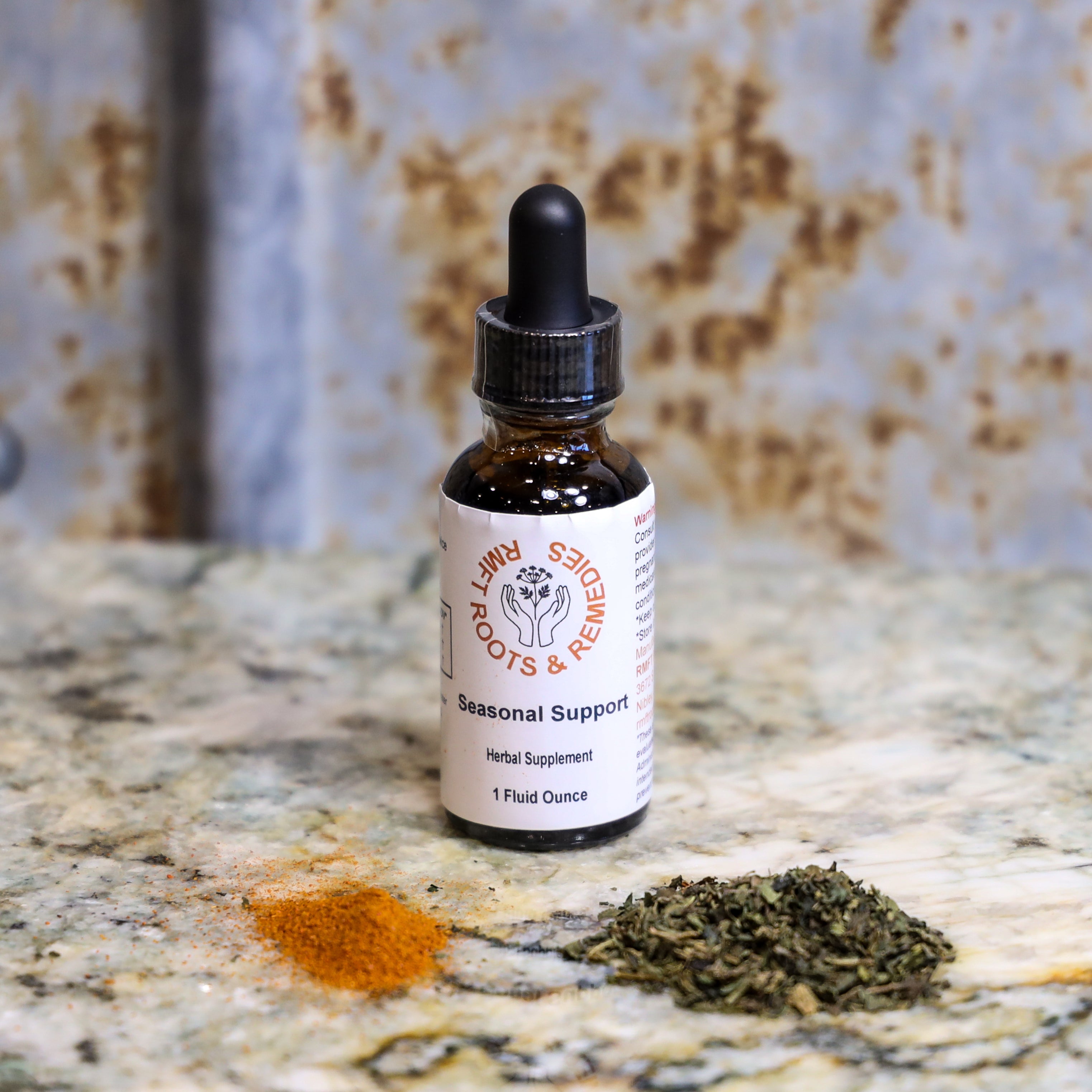 Bottle of 'Seasonal Support' tincture on a marble surface with dried herbs.