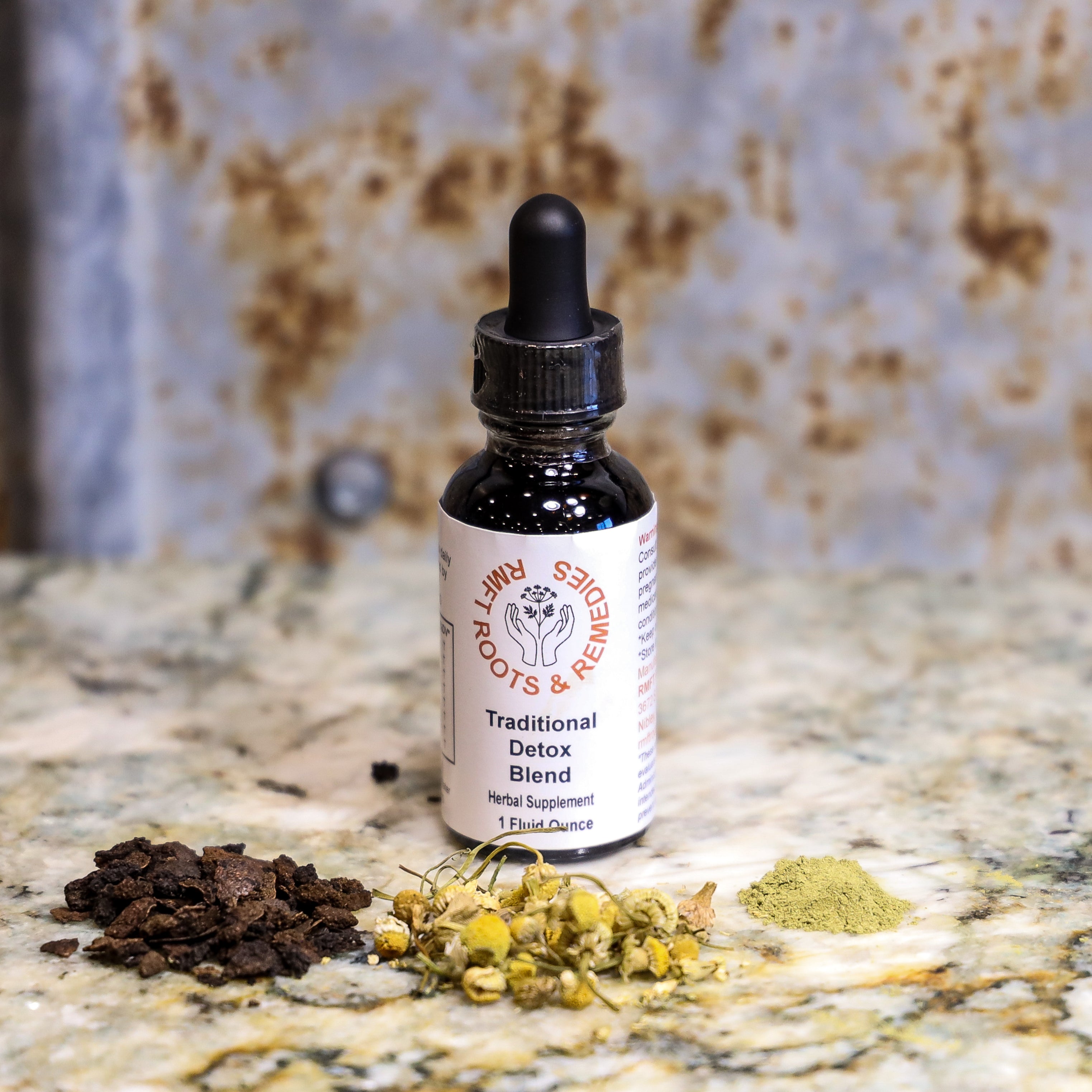 Bottle of 'Traditional Detox Blend' on a marble surface with dried herbs.