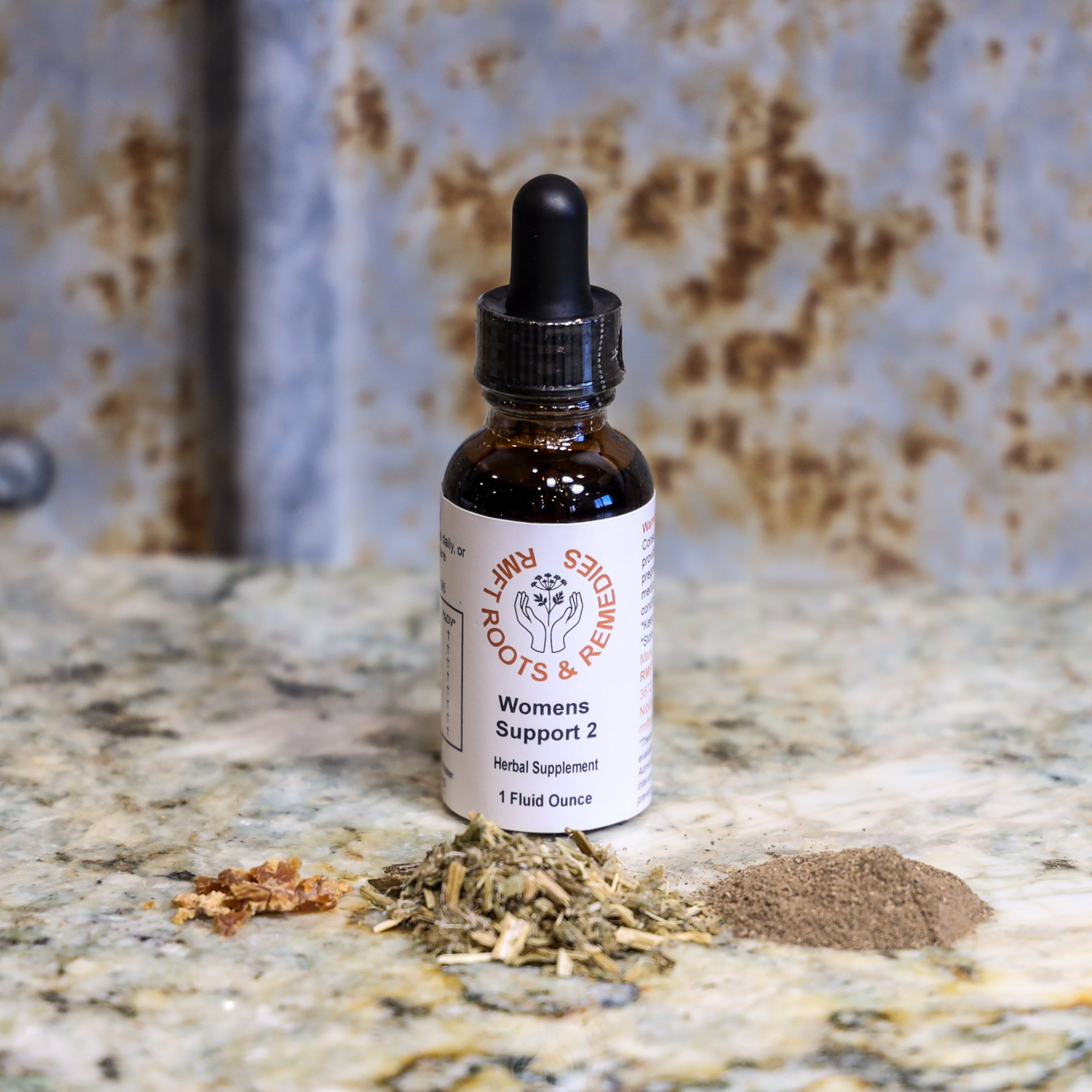 Herbal supplement bottle labeled 'Womens Support 2' on a textured surface with dried herbs.